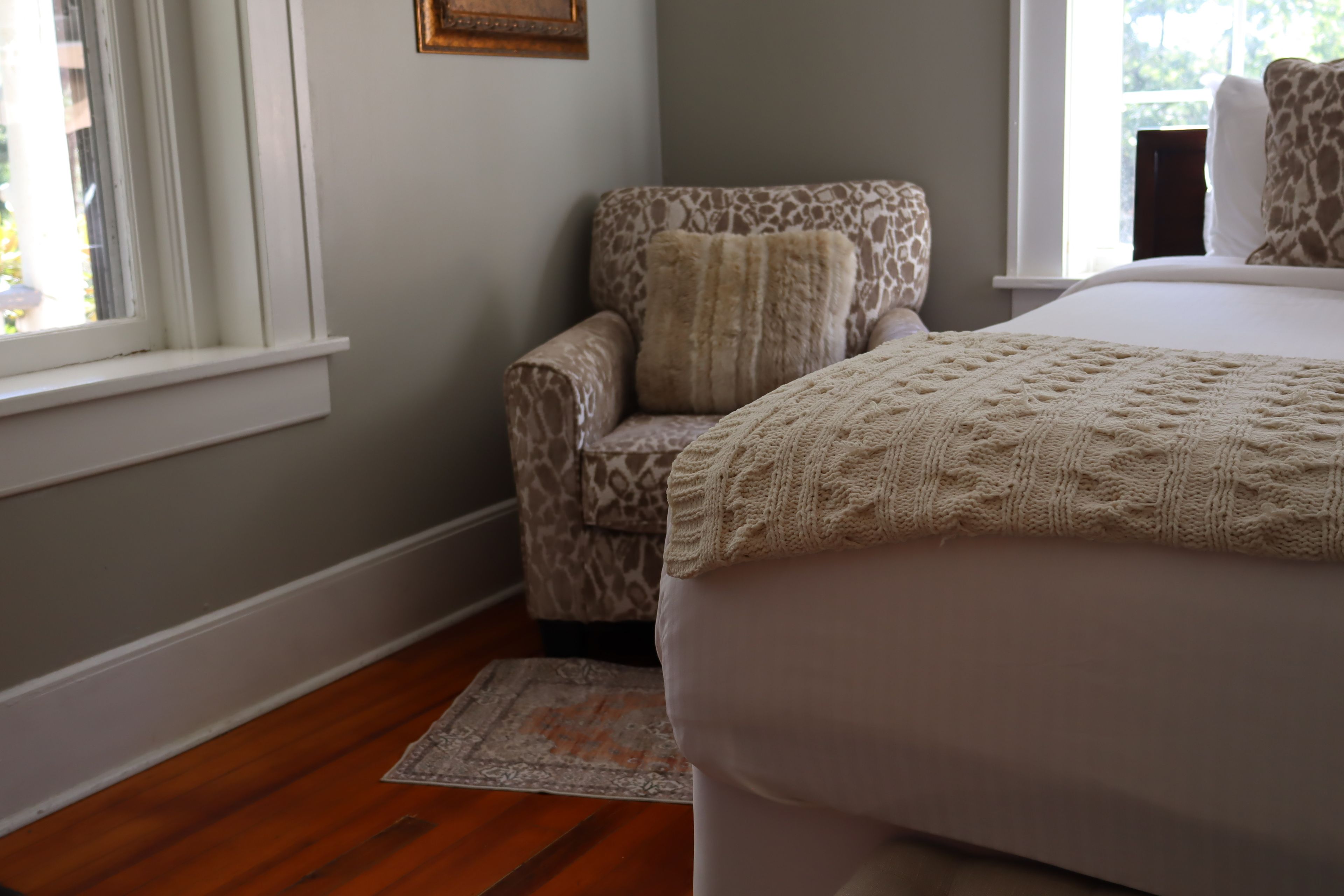 A bedroom with a bed, a chair with a patterned cushion, a window, and a rug.