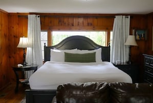 Une chambre avec un grand lit, des murs en bois, une fenêtre avec des rideaux, une table de chevet avec une lampe et une commode.