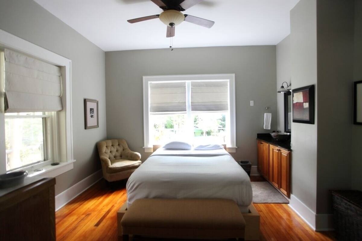 A bedroom with a bed, a chair, a desk, a ceiling fan, a window, and a television.