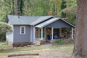 A small house with a stone foundation, a porch with a stone wall, and a covered outdoor seating area.