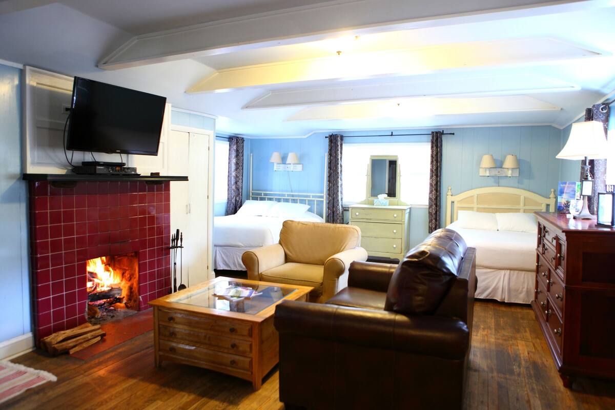 A cozy hotel room with a fireplace, a television, a bed, a sofa, and a dresser.