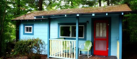 A small, single-story cabin with a red door and a porch.