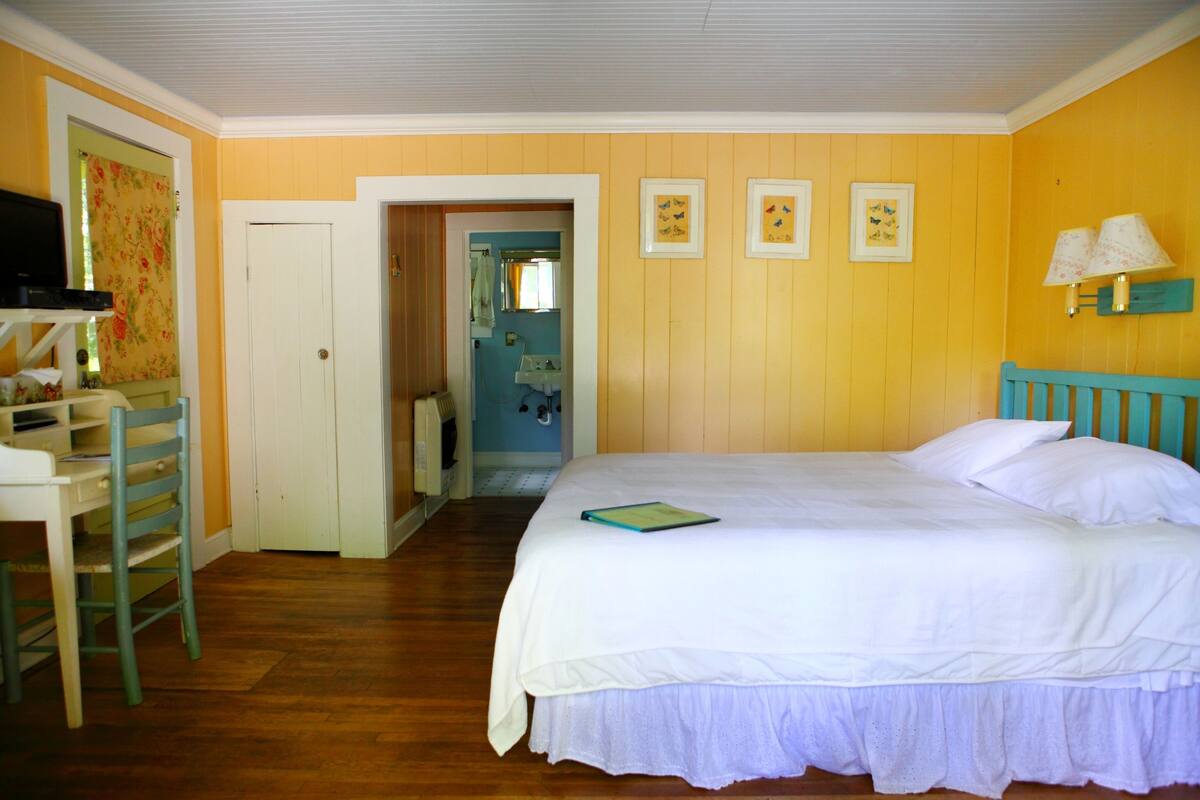 A bedroom with a bed, a desk, and a chair. There is a door leading to a bathroom.