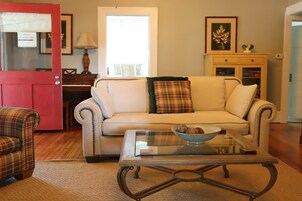Una sala de estar con sofá, sillones, una mesa de centro, un piano y un mueble.