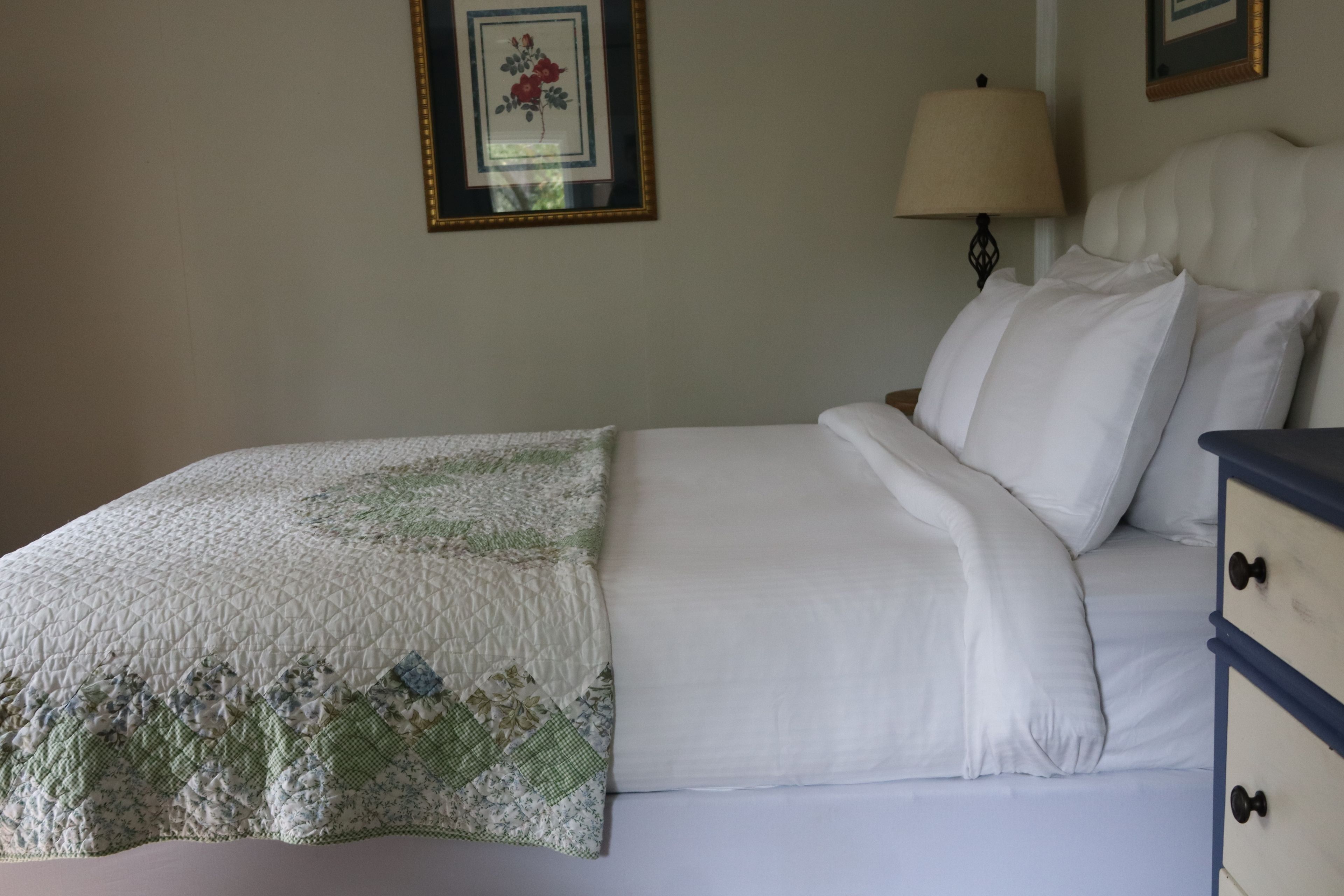 A bed with a quilt, a bedside lamp, and a dresser with drawers.