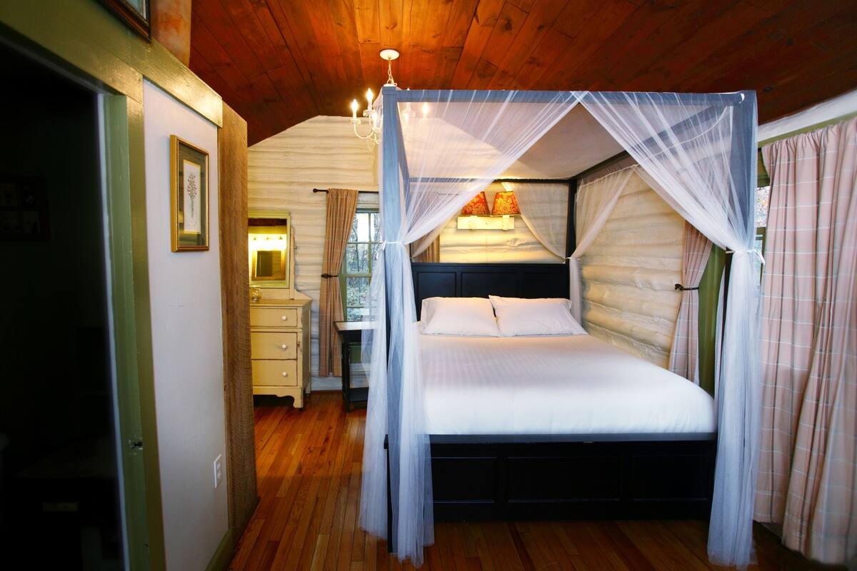 A four-poster canopy bed with a wooden headboard, a bedside table, and a nightstand.
