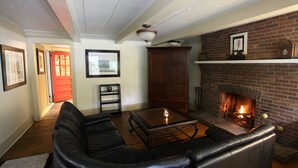 A living room with a fireplace, leather sofa, and a coffee table. - The Pines Cottages (Asheville)
