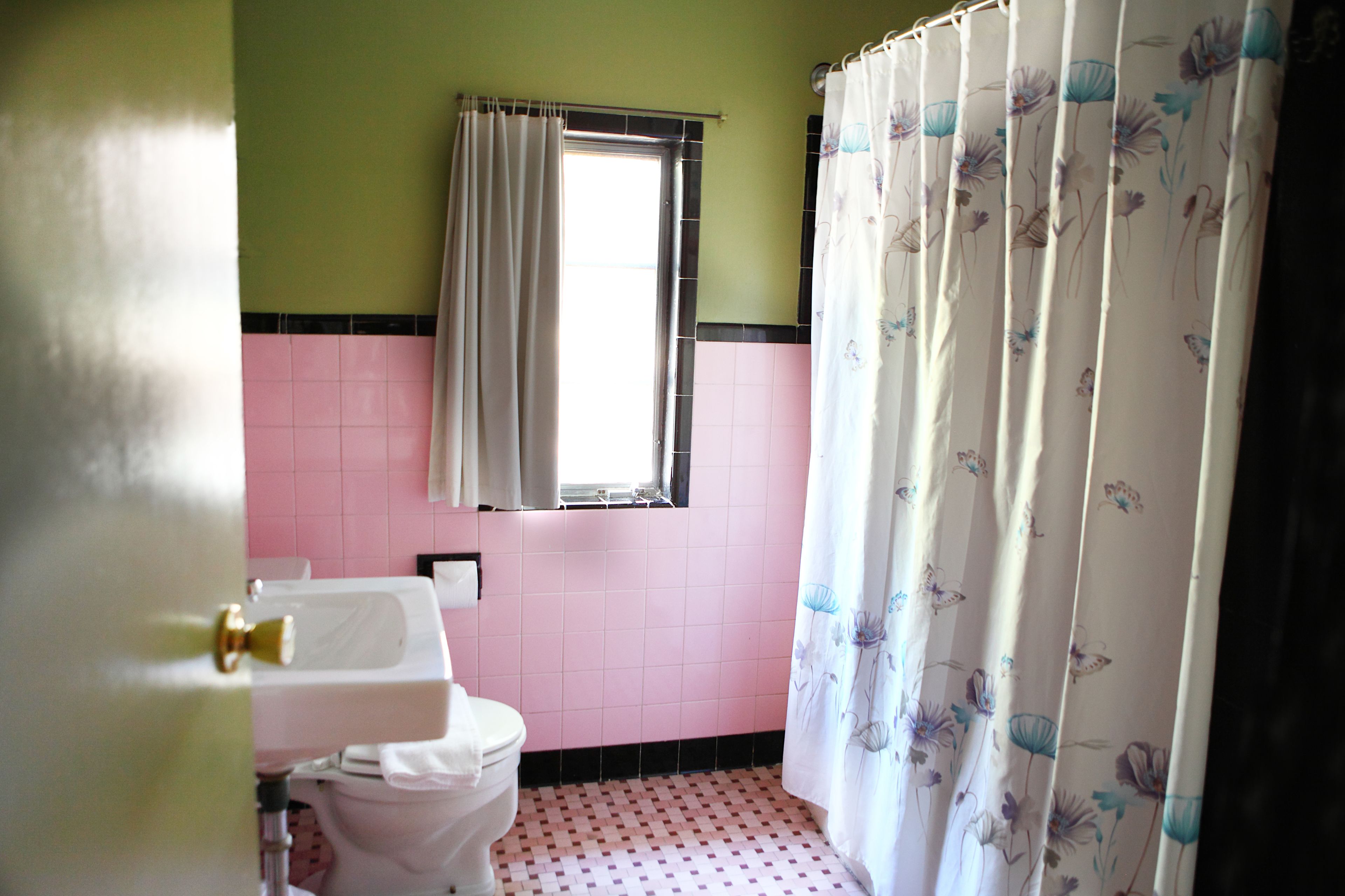Une salle de bain avec des toilettes, un lavabo et une fenêtre avec un rideau.