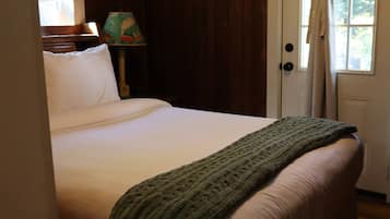 Un lit avec un matelas blanc et une couverture verte, une lampe au design coloré et une porte avec un rideau.