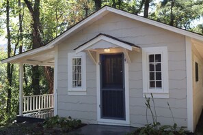 A small, single-story house with a porch, a front door, and two windows. - The Pines Cottages (Asheville)