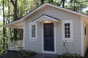 Una pequeña casa de un piso con un porche, una puerta principal y dos ventanas.