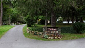 A stone sign with "The Pines" written on it, surrounded by greenery and a paved driveway. - The Pines Cottages (Asheville)