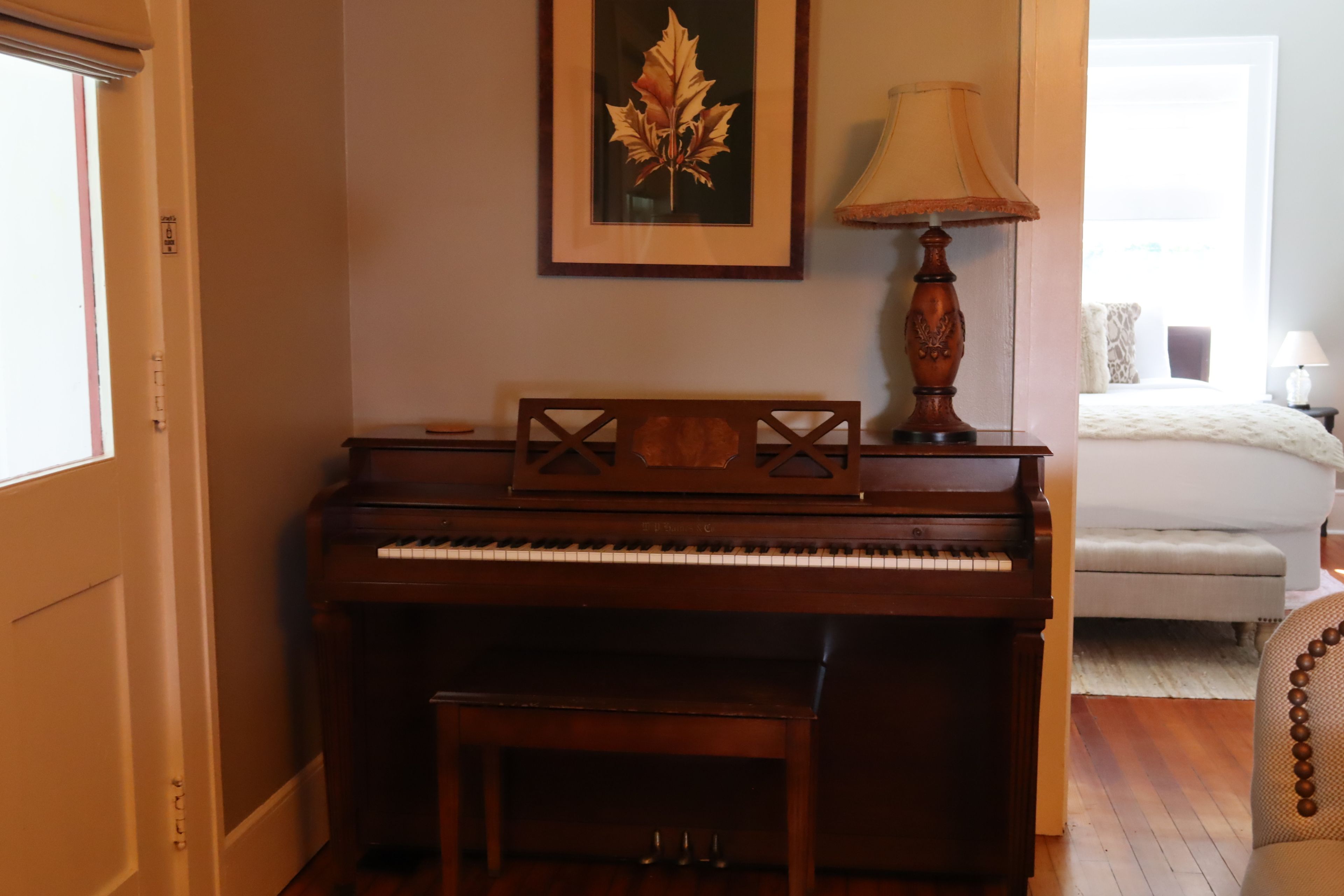 A piano in a room with a bed and a lamp.