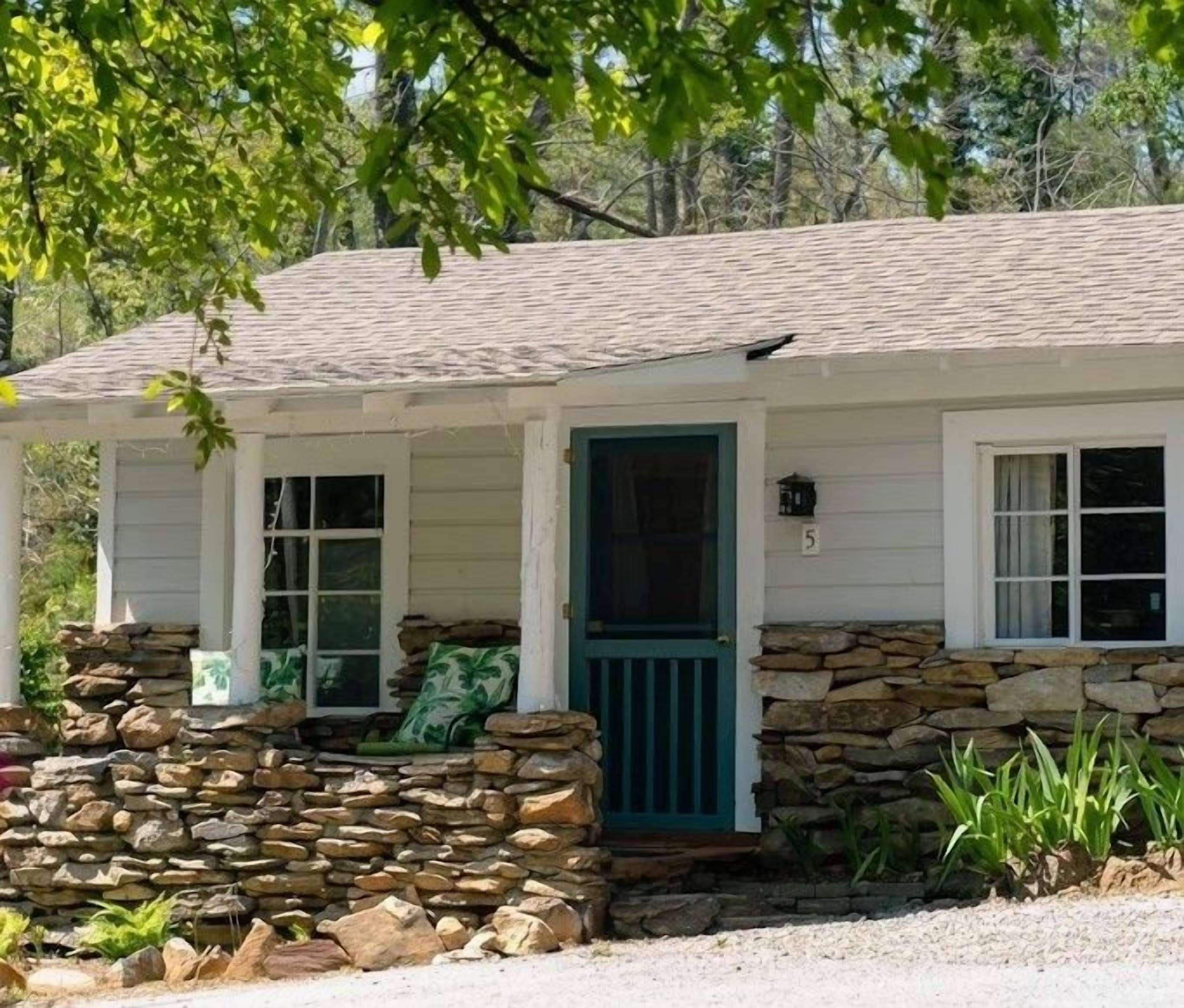 Une maison de plain-pied avec des fondations en pierre, un porche doté d’une porte verte et un panneau portant le chiffre « 5 » sur le mur.