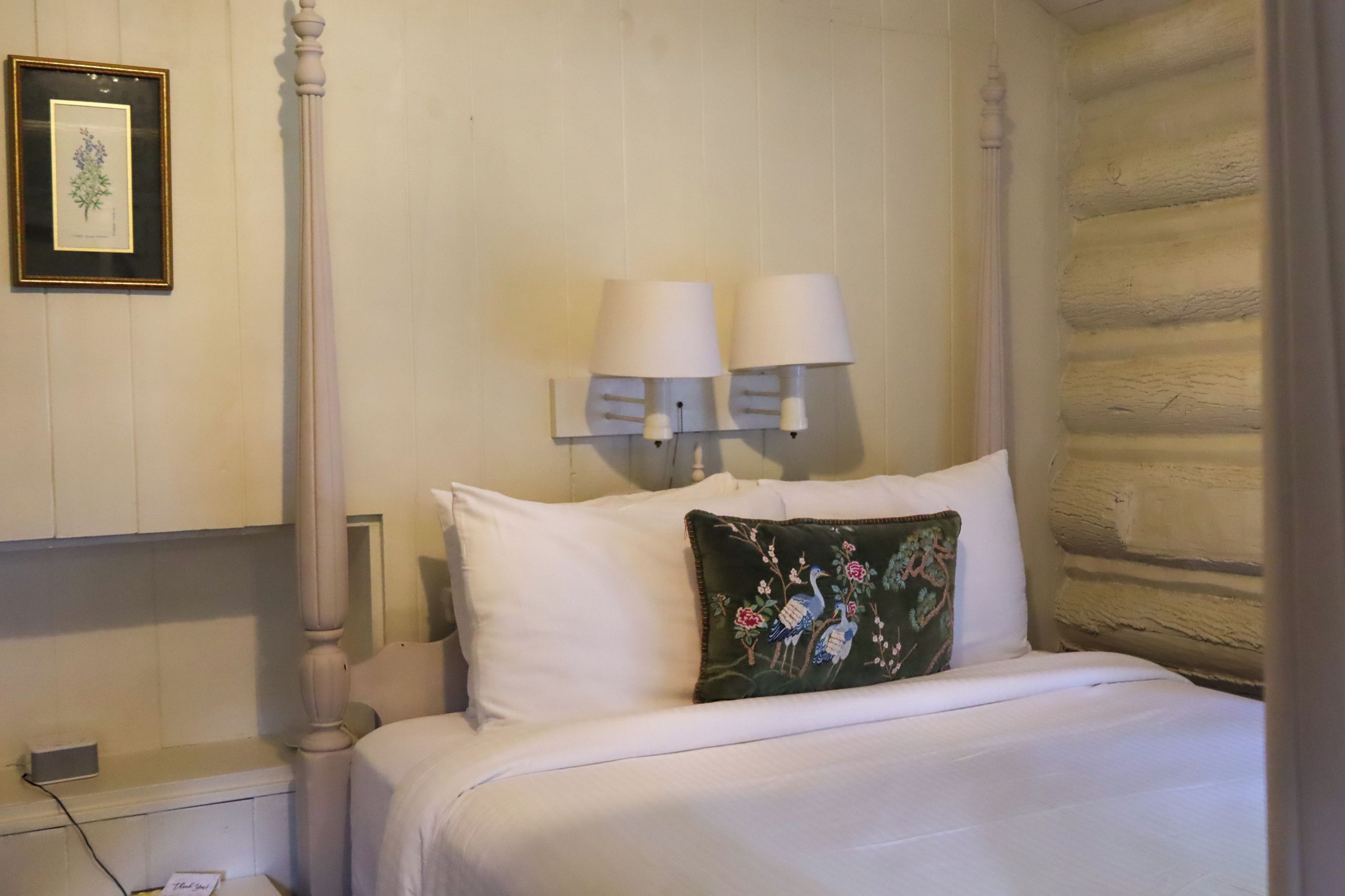 Une chambre d’hôtel avec une tête de lit en bois, un lit avec une literie blanche, un coussin décoratif et deux lampes fixées au mur.