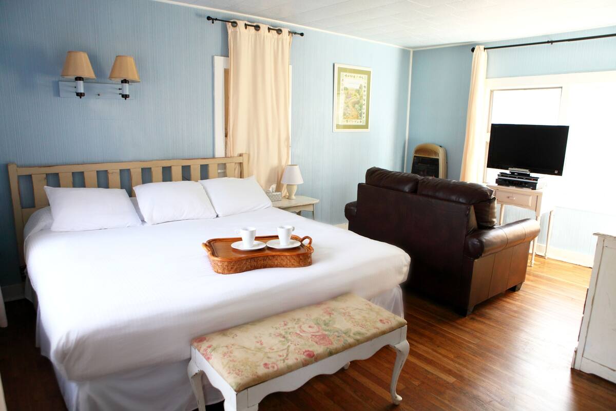 A bedroom with a bed, bedside table, lamp, TV, and a bench.