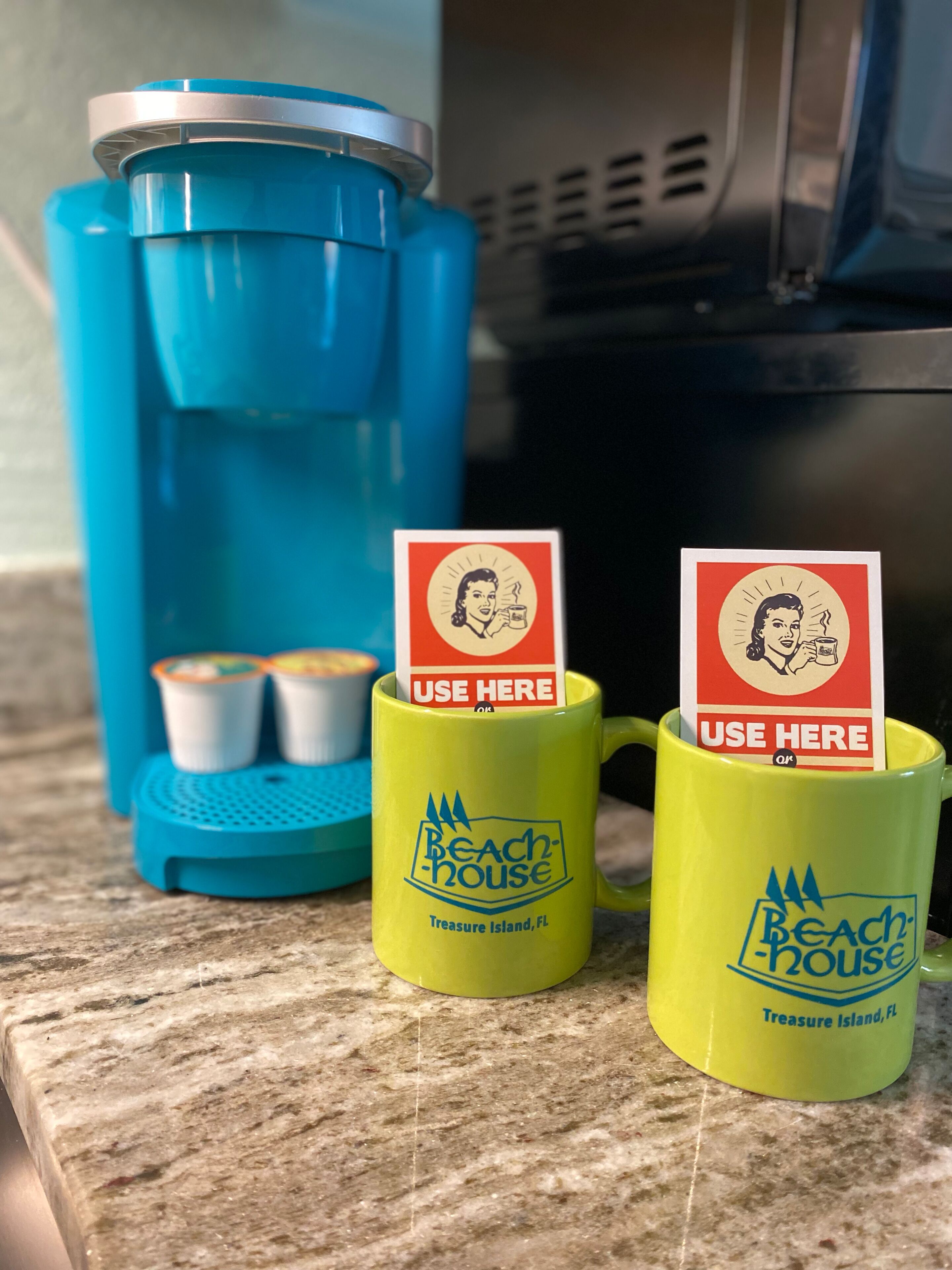 Deux tasses jaunes, ornées du logo « Beach House » et de l’inscription « Treasure Island, FL », sont posées sur un comptoir.