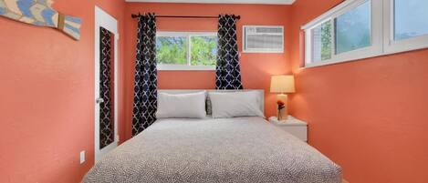 A bedroom with a bed, curtains, a nightstand with a lamp, and a window.