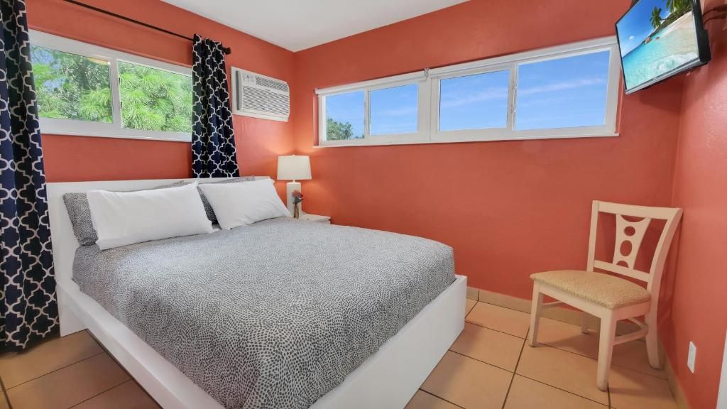 Un dormitorio con una cama, una silla, un televisor y ventanas.