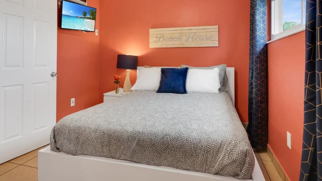 A bedroom with a bed, a nightstand, a lamp, a wall-mounted TV, and a beach-themed sign.