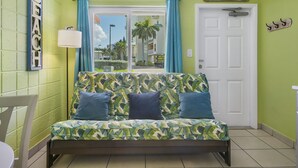 Quarto com uma cama apresentando um padrão de folhagem tropical, uma porta branca e vista para a rua.