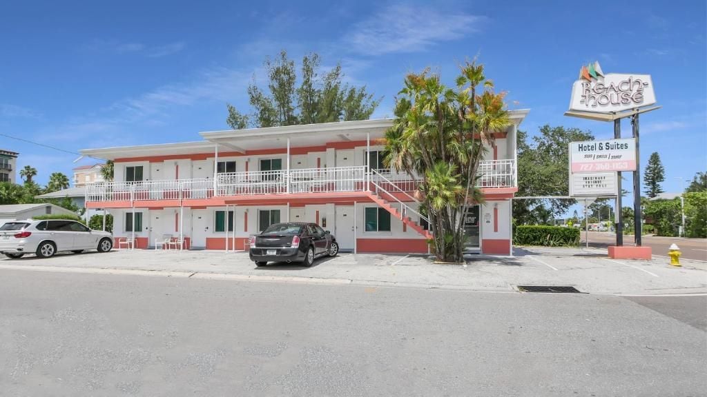 Un motel de dos pisos con fachada roja y blanca, un balcón en el segundo piso y un letrero que indica que ofrece habitaciones y suites.