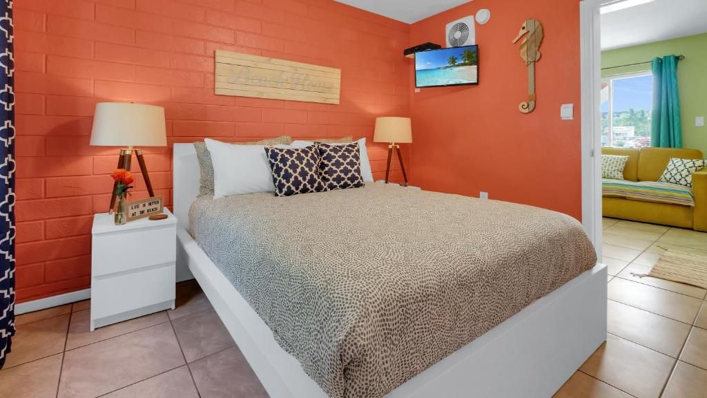 Quarto com cama, mesas de cabeceira, relógio na parede, televisão e um sofá na sala adjacente.