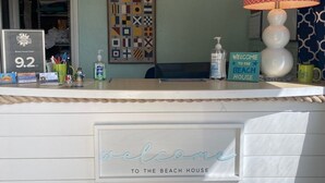 Balcão de recepção com uma placa de 'Welcome to the Beach House', arte de parede com alfabeto náutico e uma placa de premiação da casa de praia.
