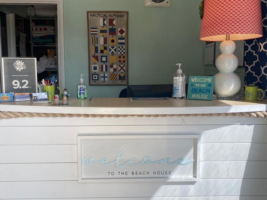 A reception desk with a 'Welcome to the Beach House' sign, a nautical alphabet wall art, and a beach house award plaque.