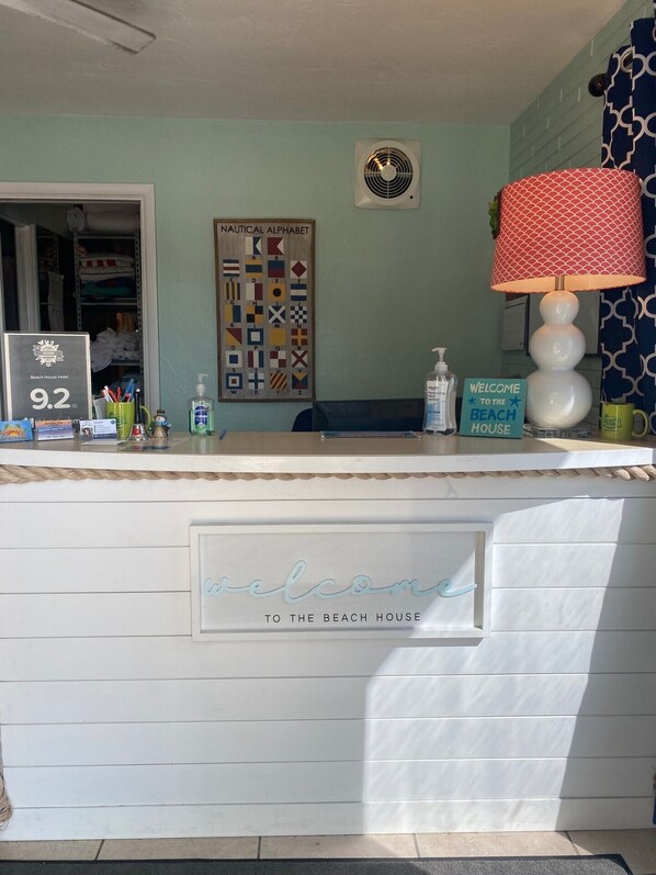A reception desk with a 'Welcome to the Beach House' sign, a nautical alphabet wall art, and a beach house award plaque.
