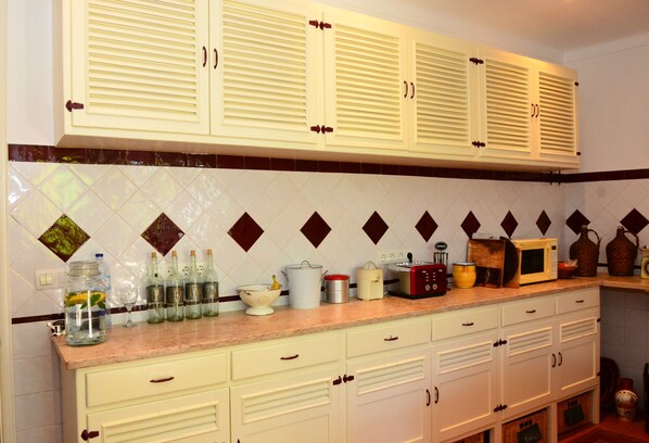 A kitchen with white cabinets, a countertop with various items, and a tiled backsplash. - Casa do Rossio (Montemor-o-Novo)