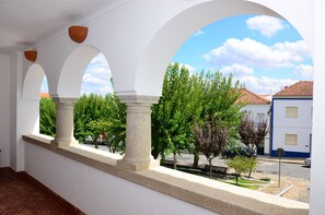 A covered outdoor area with arches and a view of trees and buildings. - Casa do Rossio (Montemor-o-Novo)