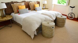 Una cama doble con varios almohadones, dos mesitas de noche con lámparas, un ventanal con vistas y dos otomanas de mimbre.