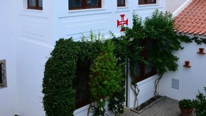 Un edificio blanco con techo de tejas, un símbolo de cruz y un pequeño jardín con plantas en macetas, una mesa y sillas blancas.