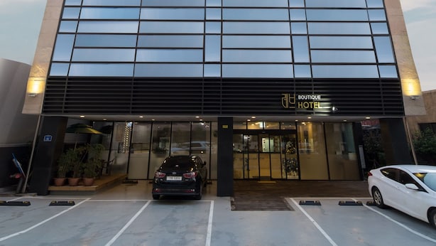 Un moderno edificio de hotel con fachada de vidrio reflectante, entrada visible y un área de estacionamiento al frente.