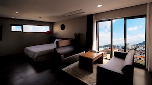 Una habitación de hotel moderna con un amplio ventanal corredero que da a un balcón, un sofá, una cama y una pequeña mesa.