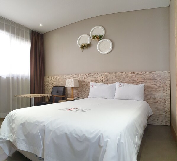 A hotel room with a large bed, a small table, a chair, and a wall-mounted lamp. - Reve Hotel Jeju (Jeju City)