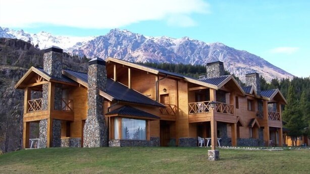 A wooden lodge with a stone chimney, multiple balconies, and a mountain backdrop.