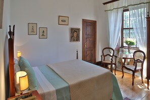 Quarto bem arrumado com uma cama, abajures, uma porta de madeira e quadros nas paredes.