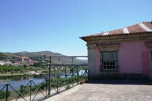 A building with a pink facade and a tiled roof overlooking a river with a bridge in the background. - Casa dos Varais (Lamego)