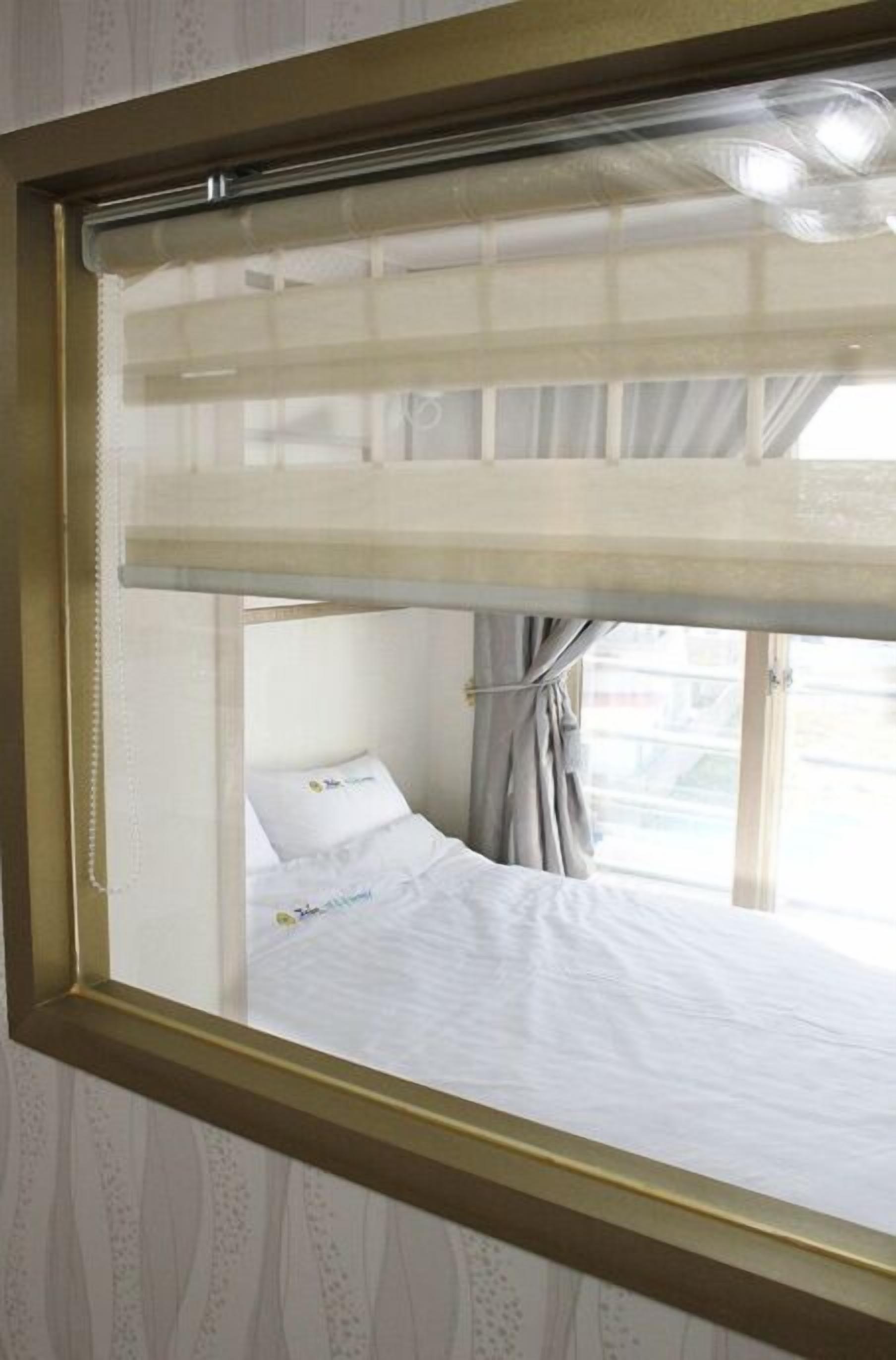 Una habitación con cama, una ventana con cortina y un espejo con marco dorado.