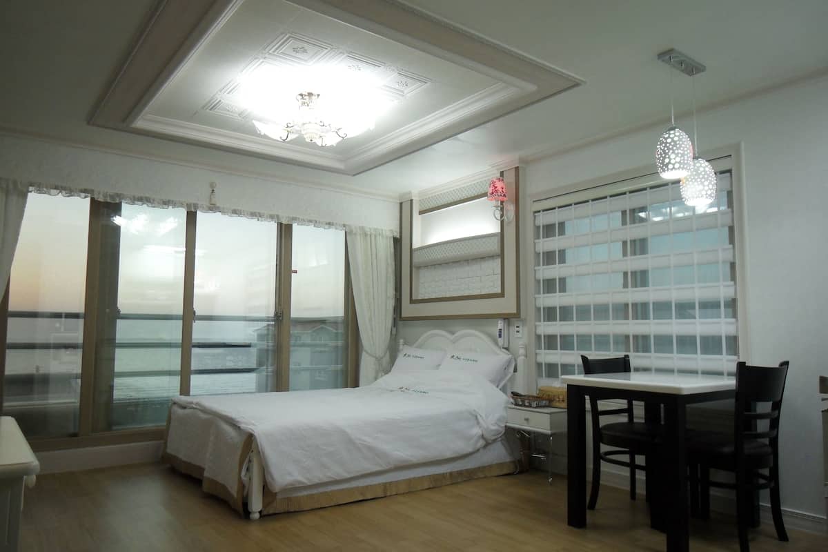 A bedroom with a bed, bedside table, and a view of the sea through large windows.