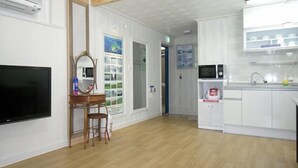 A room with a flat-screen TV, a wooden chair, a small table with a mirror, a microwave, and a sink with a soap dispenser. - Jaju Olle Pension (Jeju City)