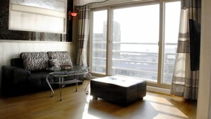 A modern living room with a black sofa, a glass coffee table, and a large window with curtains. - Jaju Olle Pension (Jeju City)