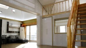 A spacious living area with a wooden staircase, a sofa, and a dining table. - Jaju Olle Pension (Jeju City)