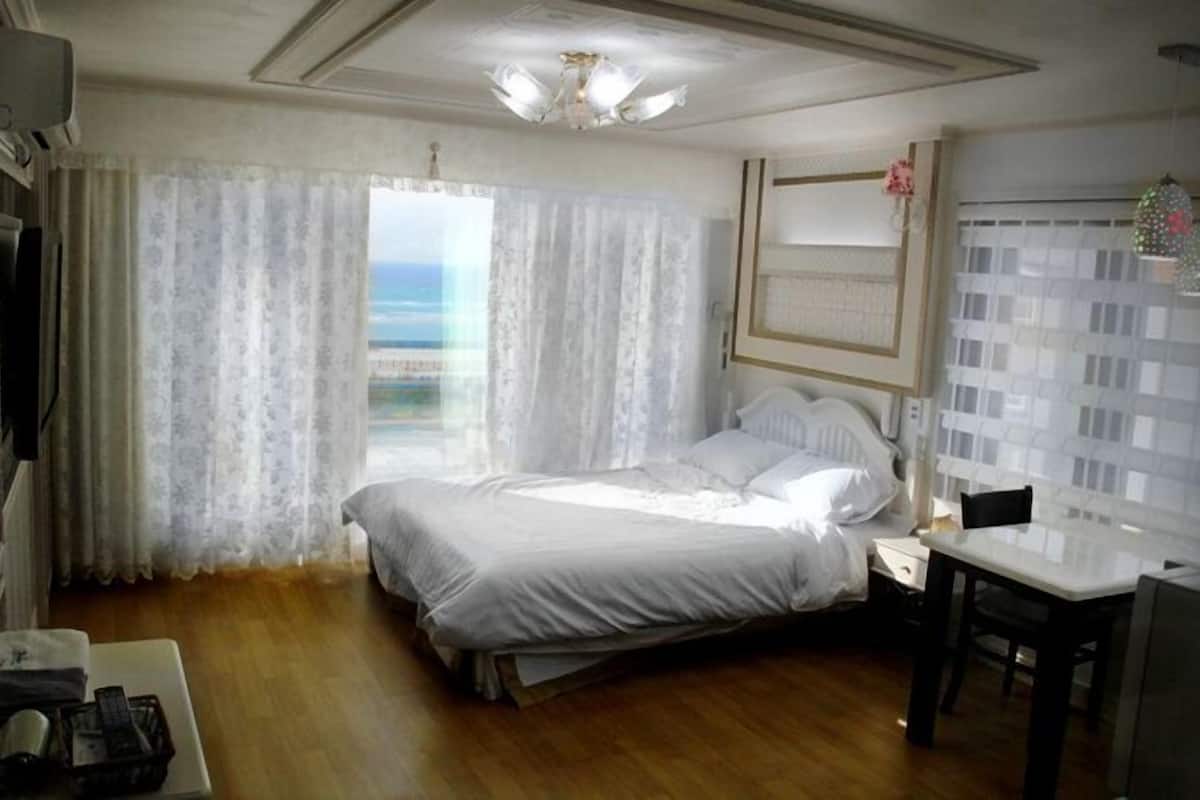 A hotel room with a bed, a desk, and a view of the sea.