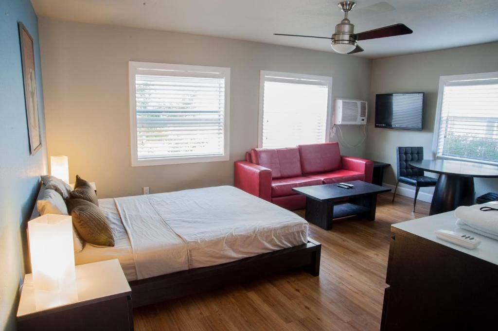 A modern hotel room with a bed, a red sofa, a small table, and a TV.