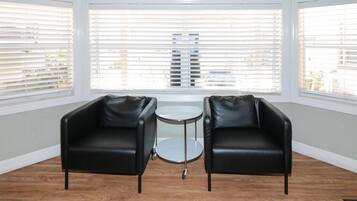 A room with two black leather chairs, a small round table, and large windows with blinds.