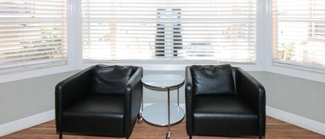 Una habitación con dos sillones de cuero negro, una mesita redonda y ventanas amplias con persianas.