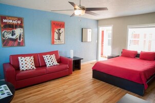 A modern bedroom with a red bed, a red sofa, and a ceiling fan.